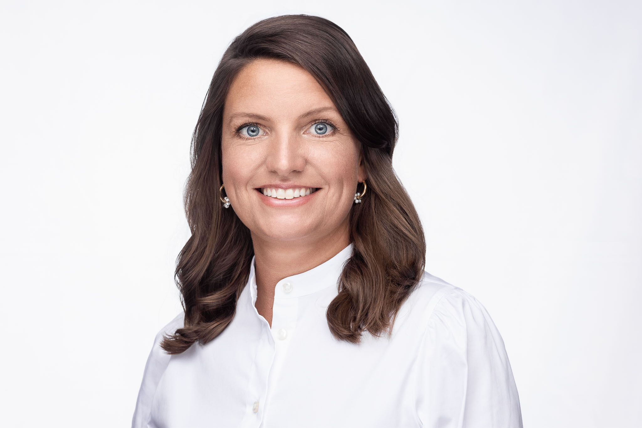 Dr. Carolin Schmidt mit weißen Kittel und offenen Haaren lächelt freundlich vor hellem Hintergrund in die Kamera.