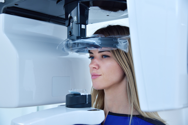 Patientin steht im Röntgengerät, während eine Aufnahme für die zahnmedizinische Untersuchung vorbereitet wird.