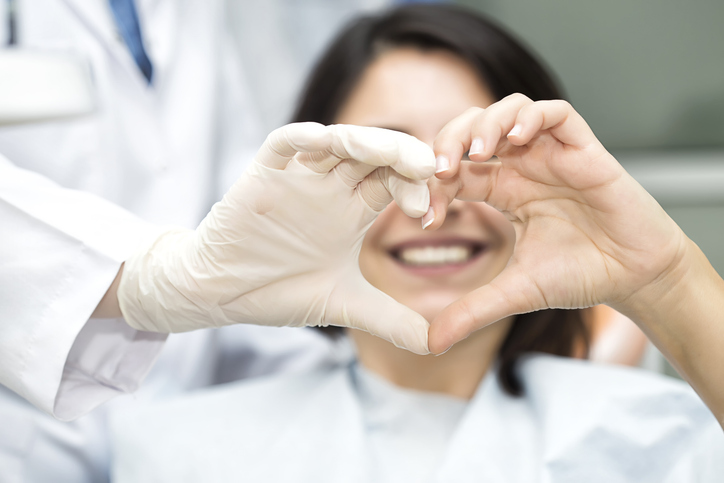 Heart Shape with doctor Patientin sitzt im Behandlungsstuhl, formt mit den Händen ein Herz und lächelt zufrieden in die Kamera.