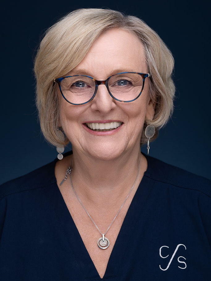 Frau Townsend, Verwaltung & Patientempfang – Porträt einer lächelnden Frau mit Brille in dunkelblauer Praxisbekleidung.